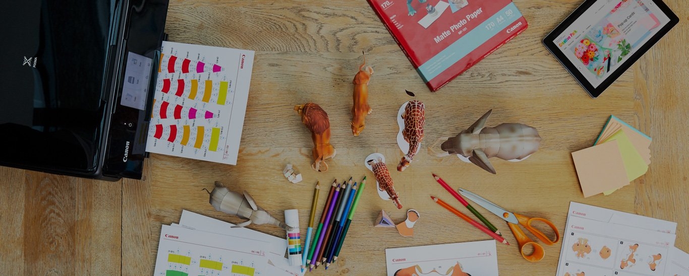 A Canon printer surrounded by templates for paper animals, coloured pencils, glue and a pair of scissors.